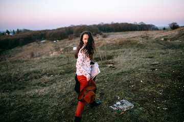 Stylish traveler woman with hat holding map on top of mountains, emotional happy moment, travel concept, space for text. Girl  walking along the grass at the top of the mountain in sunset