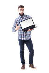 Stylish bearded young man pointing finger on blank laptop screen looking at camera. Full body isolated on white background. 