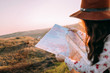 © Oleksandr - Traveler beautiful girl with a hat looking at a map holding in her hand binoculars at sunset sitting on a background of mountains. She selects a place on the map. Concept photo travel, adventure