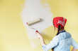 Beautiful girl in red Headband painting the wall with paint roller. Portrait of a young beautiful woman painting wall