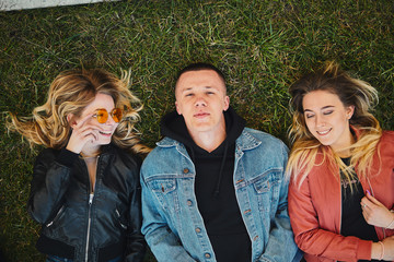 Boy with two girls on the green grass talking and smile to camera