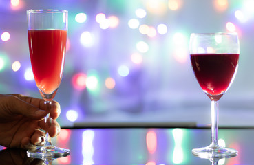 Close up view. Two wine glass is on table with a handle on one side. And background is the colorful of sparkling light bulbs.