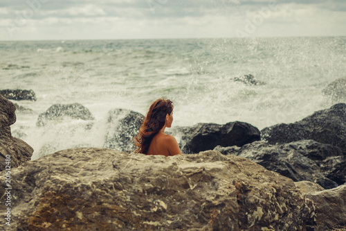 A Naked Young Girl On The Ocean Coast During A Storm Covered Herself With A Stone