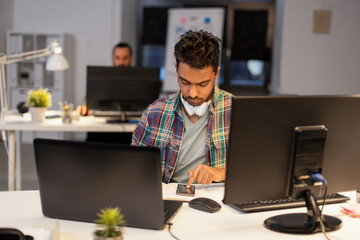 deadline, technology and people concept - creative man with smartphone and laptop computer working at night office