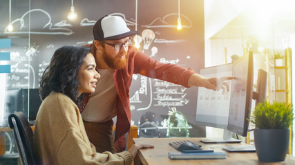 Wall Mural - at the desk beautiful man programmer helping young woman developer, pointing at the monitor, togethe