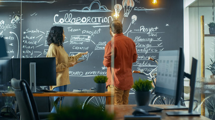 Wall Mural - female project manager holds tablet computer and shows plan drawn on a blackboard wall to male devel