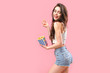 Alluring young brunette in popcorn bag looking playfully having bite on pink background.
