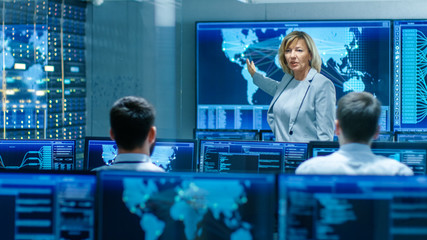 Leinwandbilder - In the System Monitoring Room Senior Female Engineer Holds Briefing For Her Subordinate Specialists, Explains Their Goals and Tasks. They Work in the High-Tech Environment.