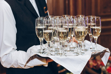 Wall Mural - waiter serving stylish golden champagne in glasses on tray. elegant glasses of alcohol drinks serving at luxury wedding reception. christmas celebration. luxury catering at feast