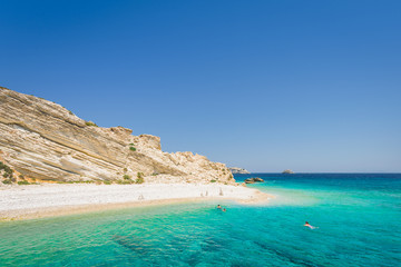 Beautiful sunny coast view to a small greek island and crystal clear blue water beach with some boats cruising and people swimming, White Island, Aspronisi, Leros, Dodecanese/ Greece – July 22 2017