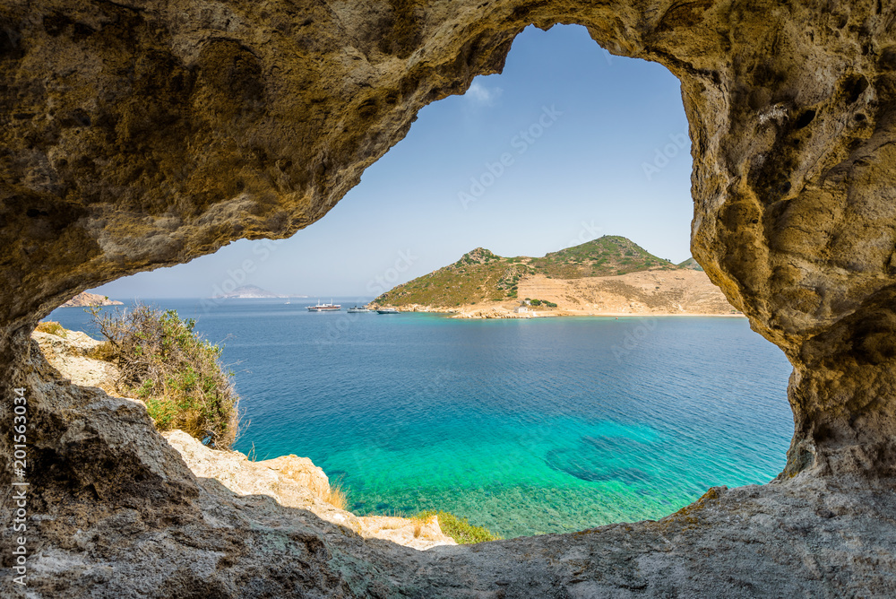 Obraz na płótnie Beautiful sunny view through a rocky cave to the greek blue sea with crystal clear water from an a hill with boats cruising fishing surrounded by mountains, Patmos Island, Kos, Dodecanese/ Greece  w salonie