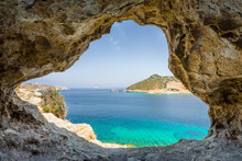 Beautiful Sunny View Through A Rocky Cave To The Greek Blue Sea With Crystal Clear Water From An A Hill With Boats Cruising Fishing Surrounded By Mountains, Patmos Island, Kos, Dodecanese/ Greece 