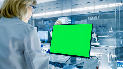 Wall Mural - female scientist working on her computers (mock-up green screen) in modern laboratory. various shelv