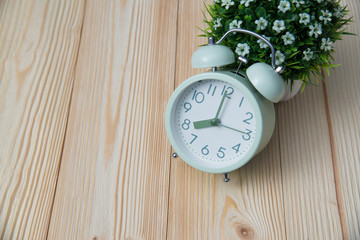 Wall Mural - Little decorative tree and flower bouquet in white vase with vintage alarm clock on wooden table with copy space.