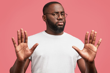 Wall Mural - Photo of serious young African American male denies something, expresses his refusement, poses against pink background, rejects participaiting in discussion, has confident look. I don`t want it!