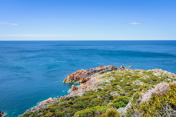 Stunning view from bright white light station to deep blue sea ocean bay turquoise water with orange red rocks at shore coast on warm sunny clear sky day, Rocky Cape National Park, Tasmania, Australia