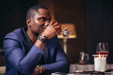 Wall Mural - Handsome afroamerican man in blue jacket drinking wine at restaurant