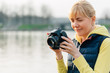 © beatleoff - Girl with professional camera in hands. Close up of female photographer in park. Pretty smiling blonde woman looking at the screen of camera