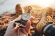 Compass closeup in a traveler hand. POV view of hiking boots. Blurred background. Flare effect