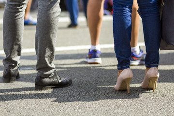 Close up of men and women legs in different shoes, high heels walking fast along the concrete road on bright sunny day. Busy lifestyle in modern city.