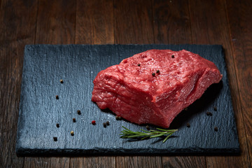 Sticker - Raw meat beef steaks on black slate board with spices and rosemary over wooden background, selective focus