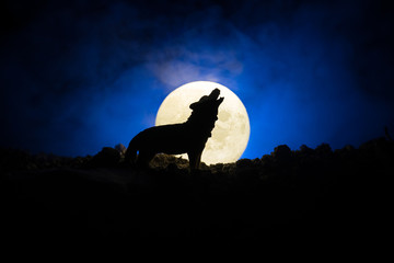 silhouette of howling wolf against dark toned foggy background and full moon or wolf in silhouette h