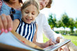 © pressmaster - Happy little girl and her parents reading book while spending time in park on summer weekend