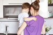 © sementsova321 - Portrait of young mother holds little son on hands, stand back together, work on kitchen, going to eat delicious dinner, takes care of her small male child. Housekeeping, children, domestic routine