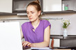© sementsova321 - Concentrated busy housewife works freelance, sits in front of opened laptop computer, surronded with business documents and calculator, makes report online, sits against cozy kitchen interior