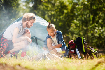 Wall Mural - Two young backpackers making bonfire by pile of woods during their backpack trip in the forest