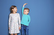 © New Africa - Little girl and boy measuring their height on color background