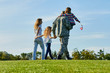 © DenisProduction.com - Back view soldier and his family are walking on the grass. Patriotic family with american flags, blue sky background.