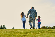 Soldier Walking With Little Girls Holding Hands. Back View, Father And Daughters Are Walking Together.