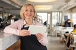 Being a waitress. Delighted aged waitress holding a tablet and smiling