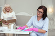 © Viacheslav Yakobchuk - Help with cleaning. Elder woman reading book while thoughtful caregiver removing dust