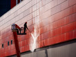© Tricky Shark - Worker wearing safety harness washes wall facade at height on modern building in a crane.