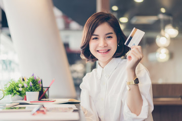 Young beautiful asian woman working on desk with tablet and showing credit card in coworking spaces.