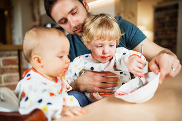 Wall Mural - Father feeding two toddlers at home.