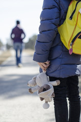  a small child holds a soft toy in his hands, and looks toward the departing mother