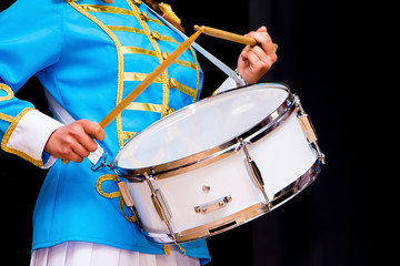 Young girl in elegant suit plays on drum. Isolated black background_