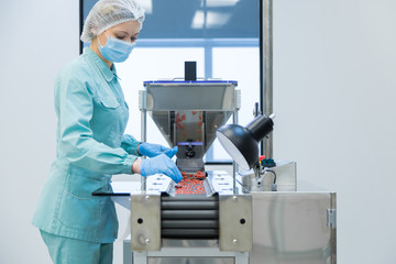 Poster - Pharmacy industry woman worker in protective clothing operating production of tablets in sterile working conditions