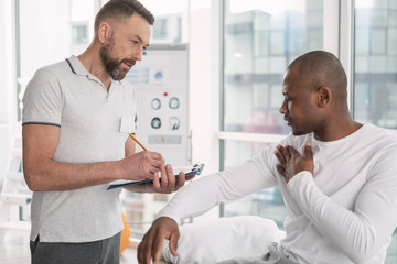 Wall Mural - Description of symptoms. Pleasant young man talking to his doctor while describing symptoms