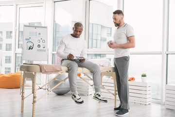 Wall Mural - Medical agreement. Serious young man sitting on the medical couch while signing a document