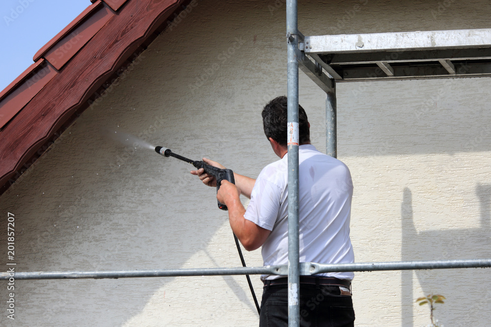 Robotnik, malarz myje karcherem ścianę, fasade budynku mieszkalnego stojąc na rusztowaniu. - obrazy, fototapety, plakaty 