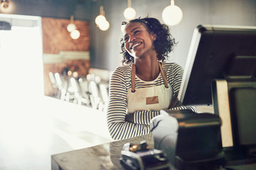 Young African waitress standing at an order terminal and laughin