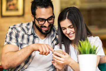 Wall Mural - Couple of office workers, bearded man in eyeglasses and brunette girl having fun watching taked pictures on smartphone