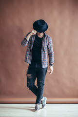 Full length portrait of a handsome man touching his hat posing on brown background