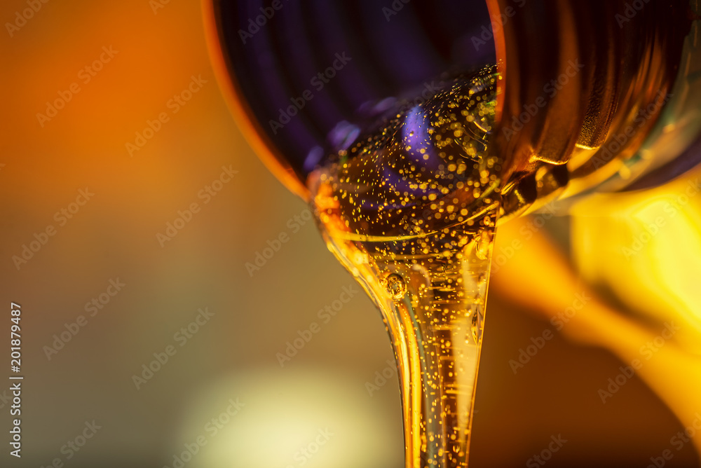 Liquid stream of motorcycle motor oil flows from the neck of the bottle close-up. - obrazy, fototapety, plakaty 