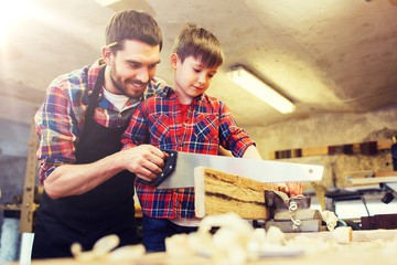 Wall Mural - family, carpentry, woodwork and people concept - father and little son with saw sawing wood plank at workshop