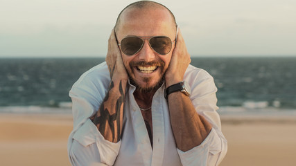 smiling and happy hipster MAN with tattoos and beard on a sandy and windy beach in spain